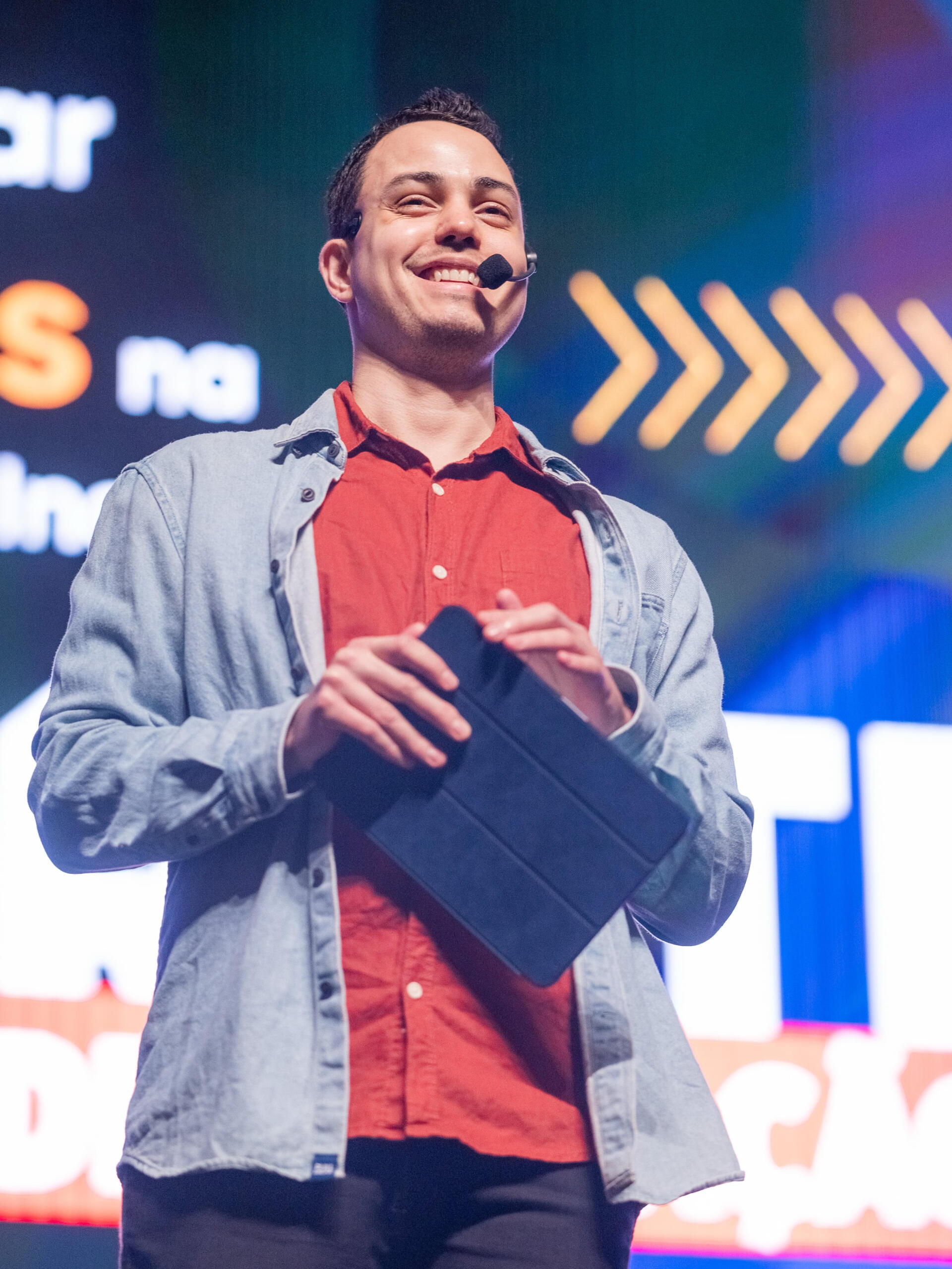 Thássius Veloso atua como apresentador e mediador de eventos Homem fala ao microfone, enquanto segura tablet