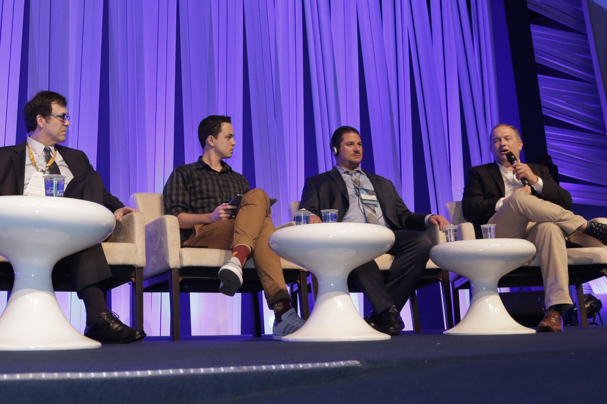 Thássius Veloso atua como apresentador e mediador de eventos Homem fala ao microfone, enquanto segura tablet